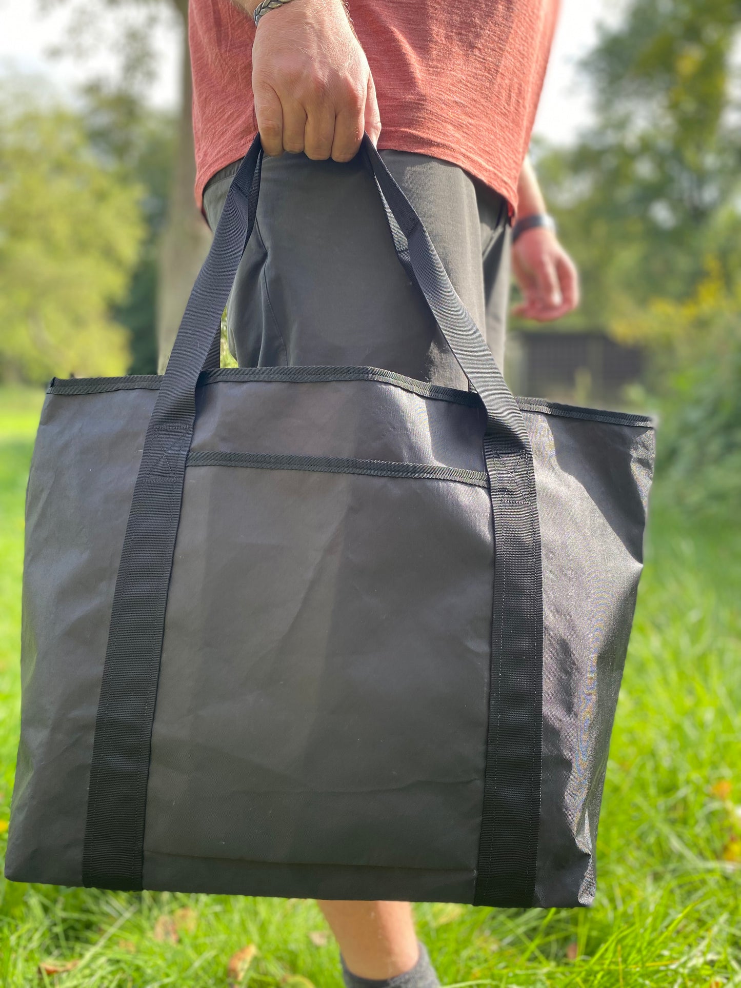 Die schwarze Tragetasche aus Ecopak wird von einem Mann getragen, der auf einer Wiese steht.